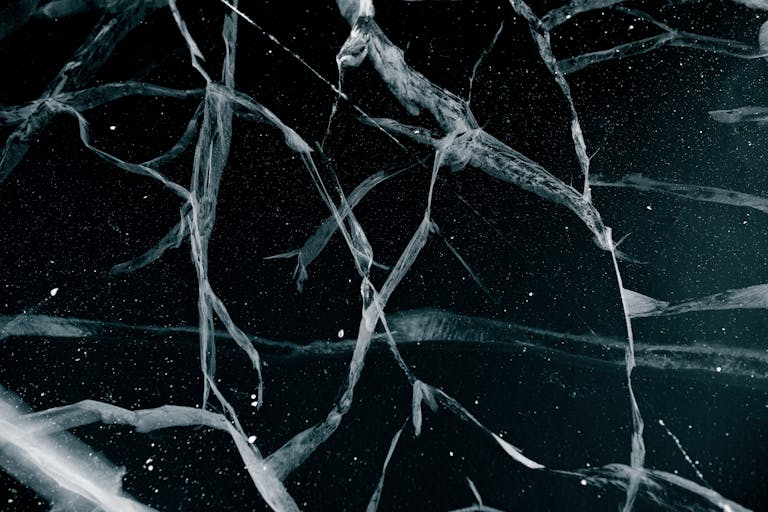 Close-up abstract view of cracked ice on a frozen lake in winter, showcasing intricate patterns.