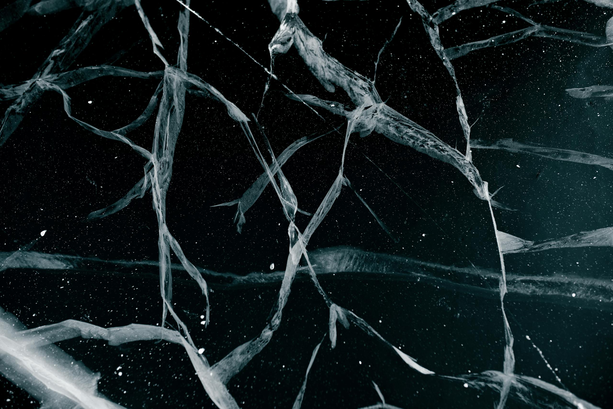 Close-up abstract view of cracked ice on a frozen lake in winter, showcasing intricate patterns.
