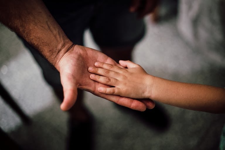 Close-up of a child's hand resting gently on a man's hand, symbolizing love and support.