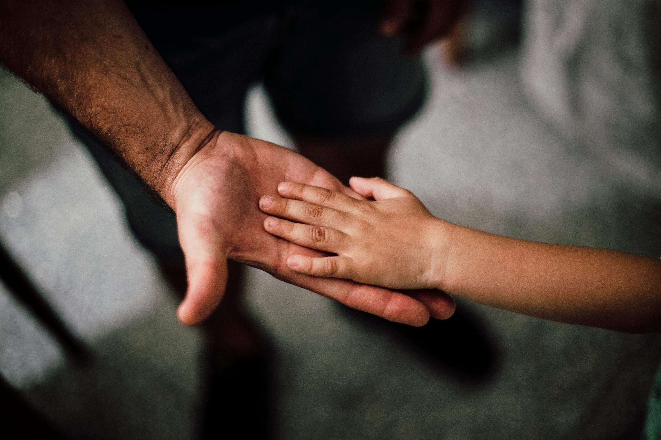 Close-up of a child's hand resting gently on a man's hand, symbolizing love and support.